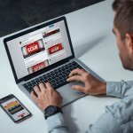 A person reviews scam-flagged financial posts on a laptop and phone, illustrating concerns over platform scam liability.