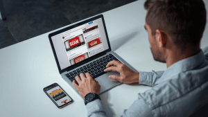 A person reviews scam-flagged financial posts on a laptop and phone, illustrating concerns over platform scam liability.
